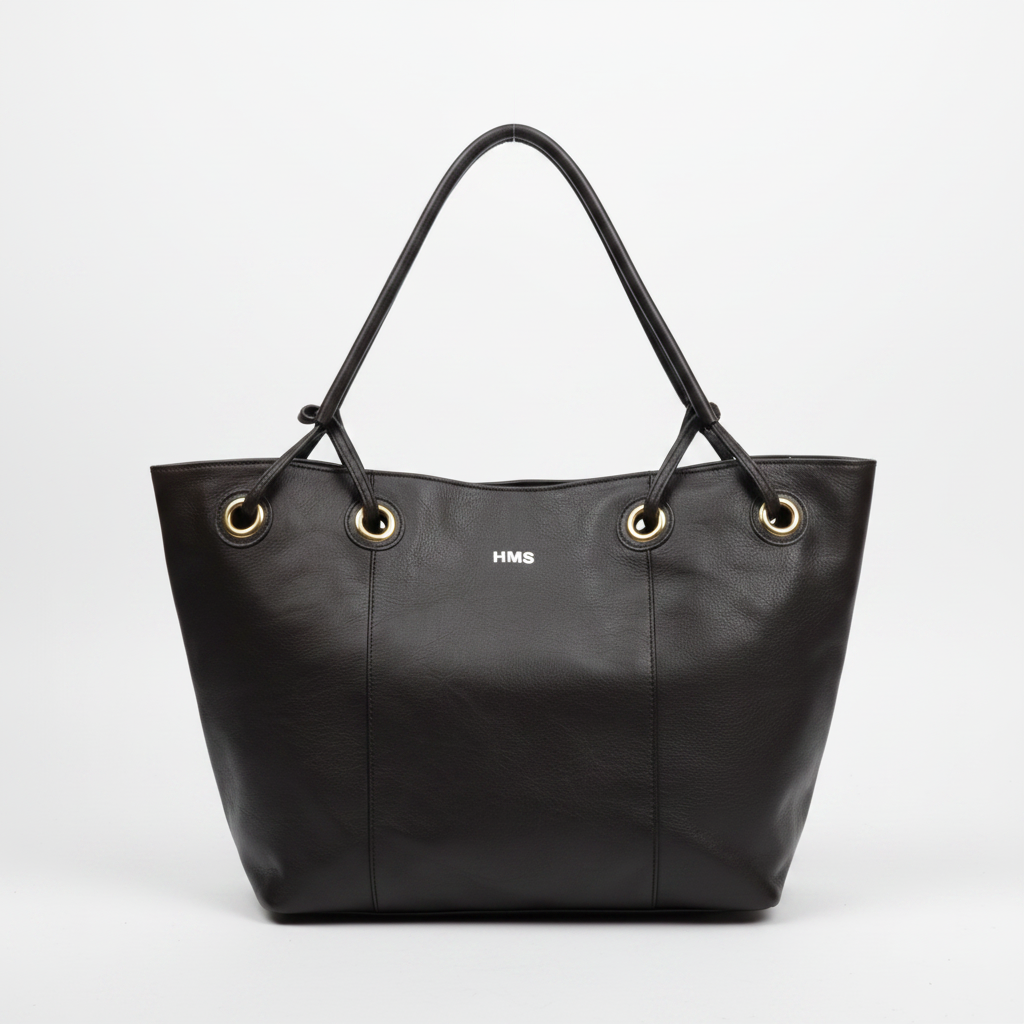 A black leather tote bag with double shoulder straps, gold-tone grommets, and a small white 'HMS' logo on the front, photographed against a clean white background.